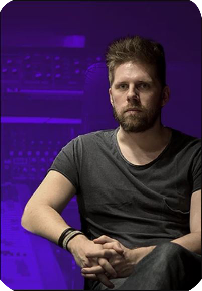 A man is sitting against a backdrop of audio tuning equipment.